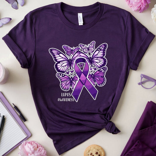 Purple t-shirt with butterfly design and lupus awareness ribbon on a light surface with flowers and glasses.