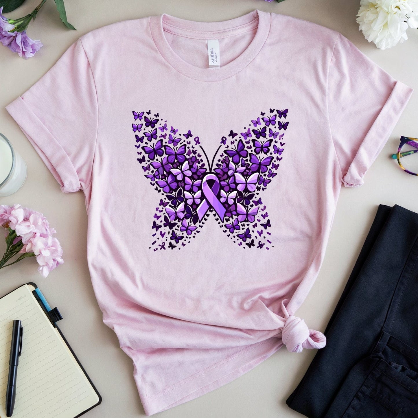 Pink t-shirt with purple butterfly design on a light surface with flowers and glasses.