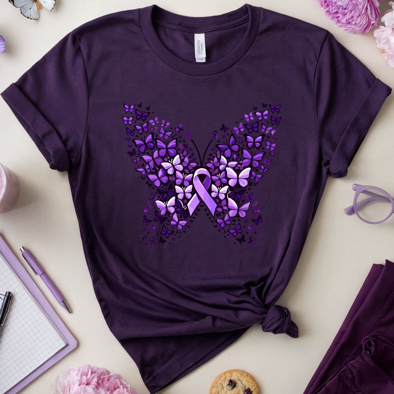 Purple t-shirt with butterfly design on a light surface with flowers and glasses.