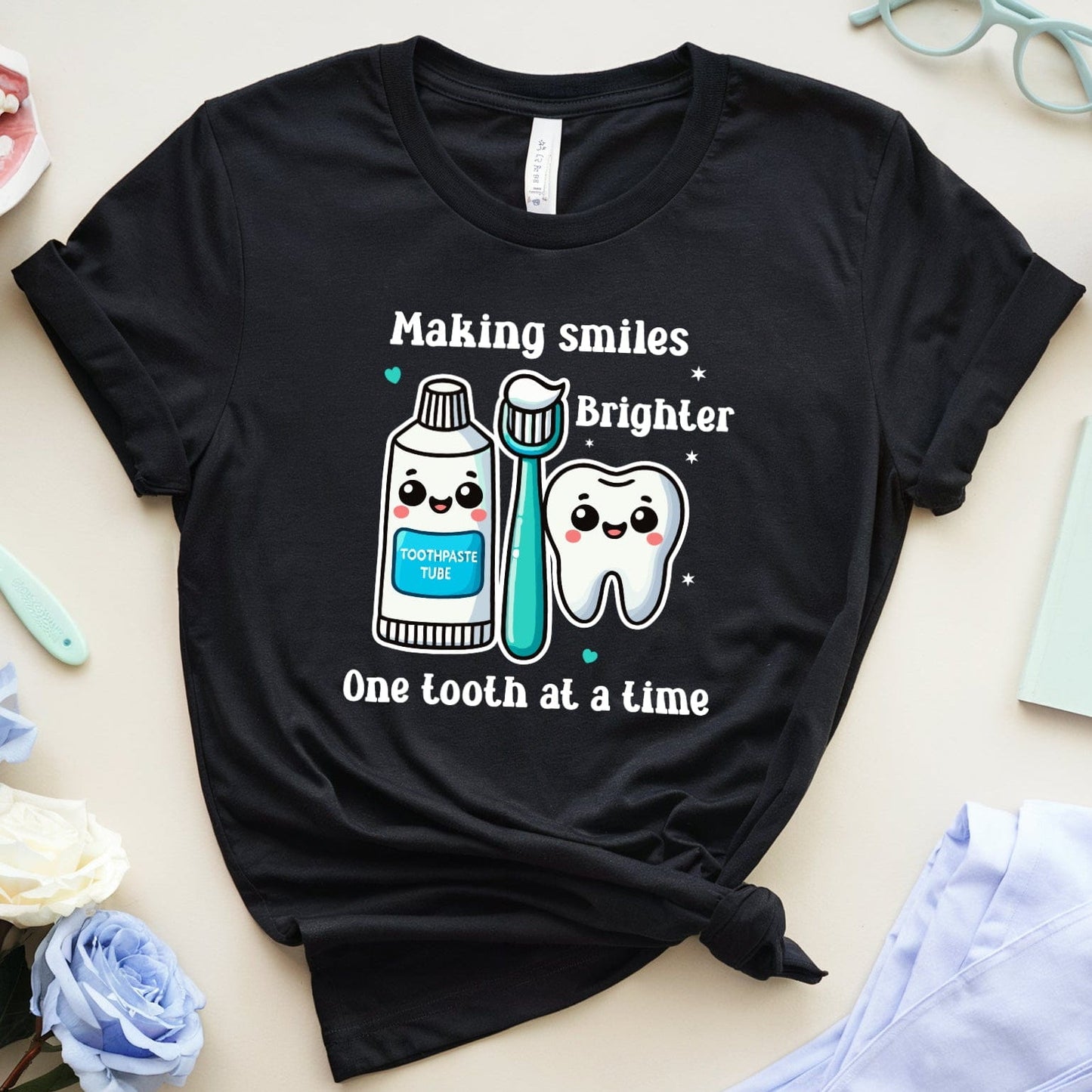 Black t-shirt with dental-themed design on a light surface with dental-themed items.