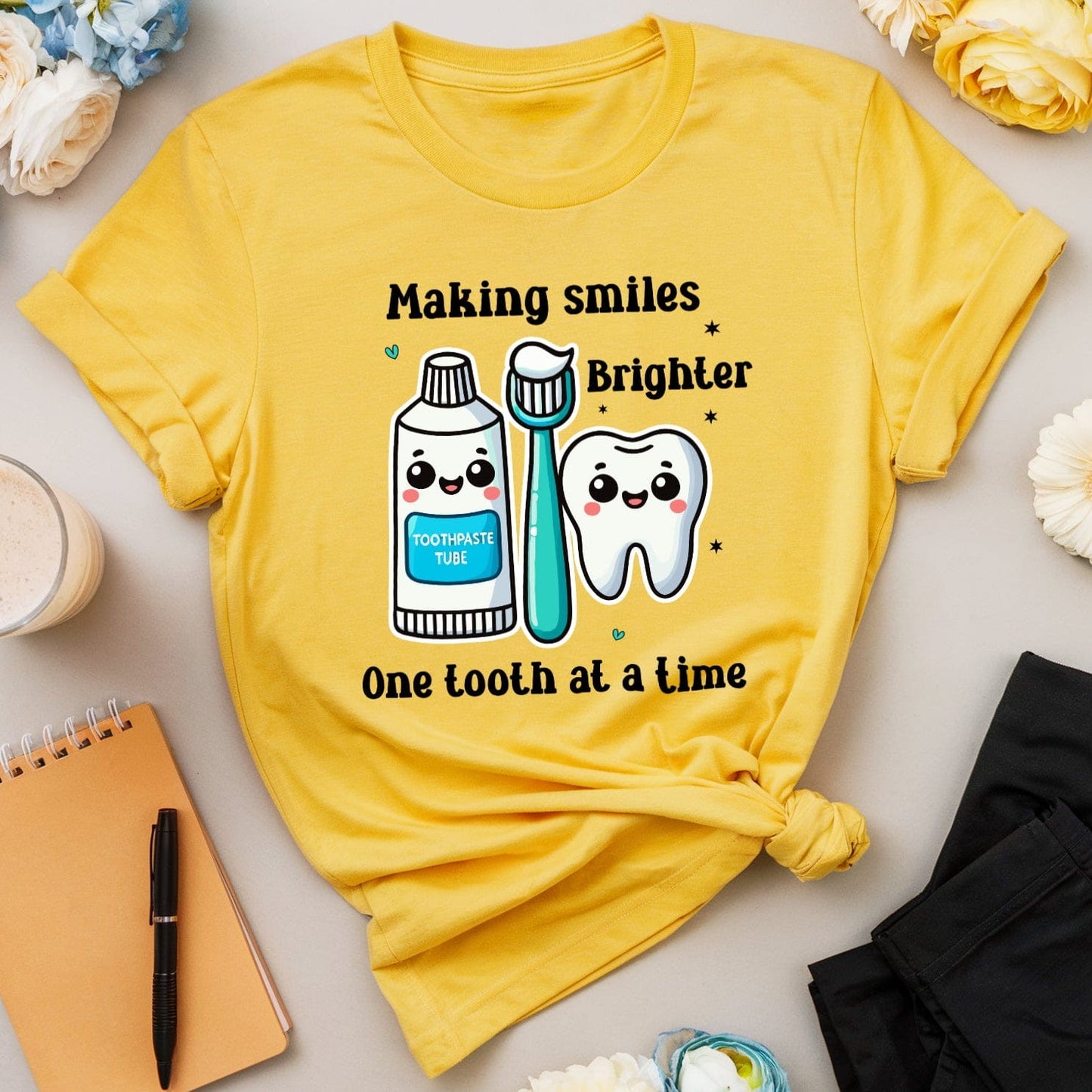 Yellow t-shirt with dental-themed design on a light surface with flowers and stationery items.
