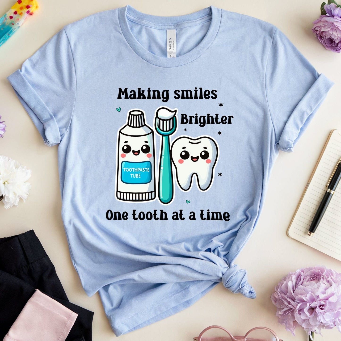 Light blue t-shirt with dental-themed design on a light surface with flowers and stationery.