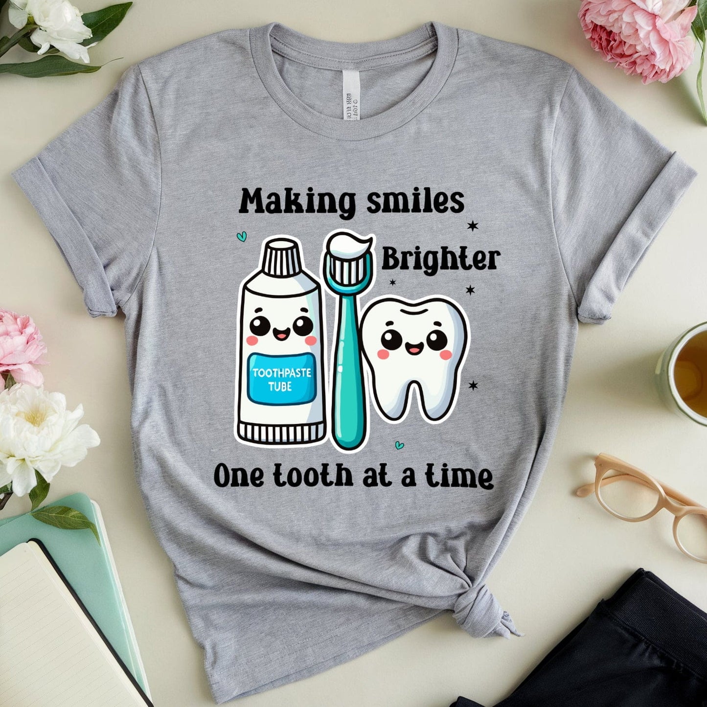 Gray t-shirt with dental-themed design on a light surface with flowers and a cup.