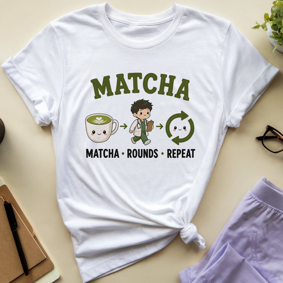A white graphic t-shirt with a 'MATCHA' design, styled in a flat lay on a beige background with a coffee cup, notebook, glasses, and lavender shorts.