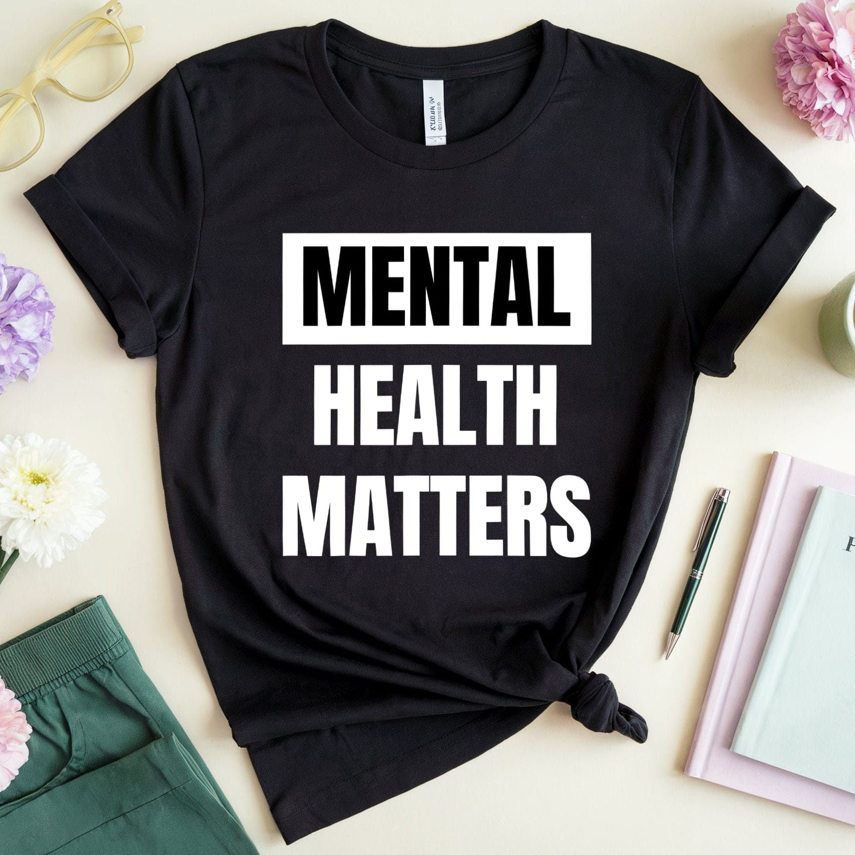 Black t-shirt with 'Mental Health Matters' text on a table with flowers and books.