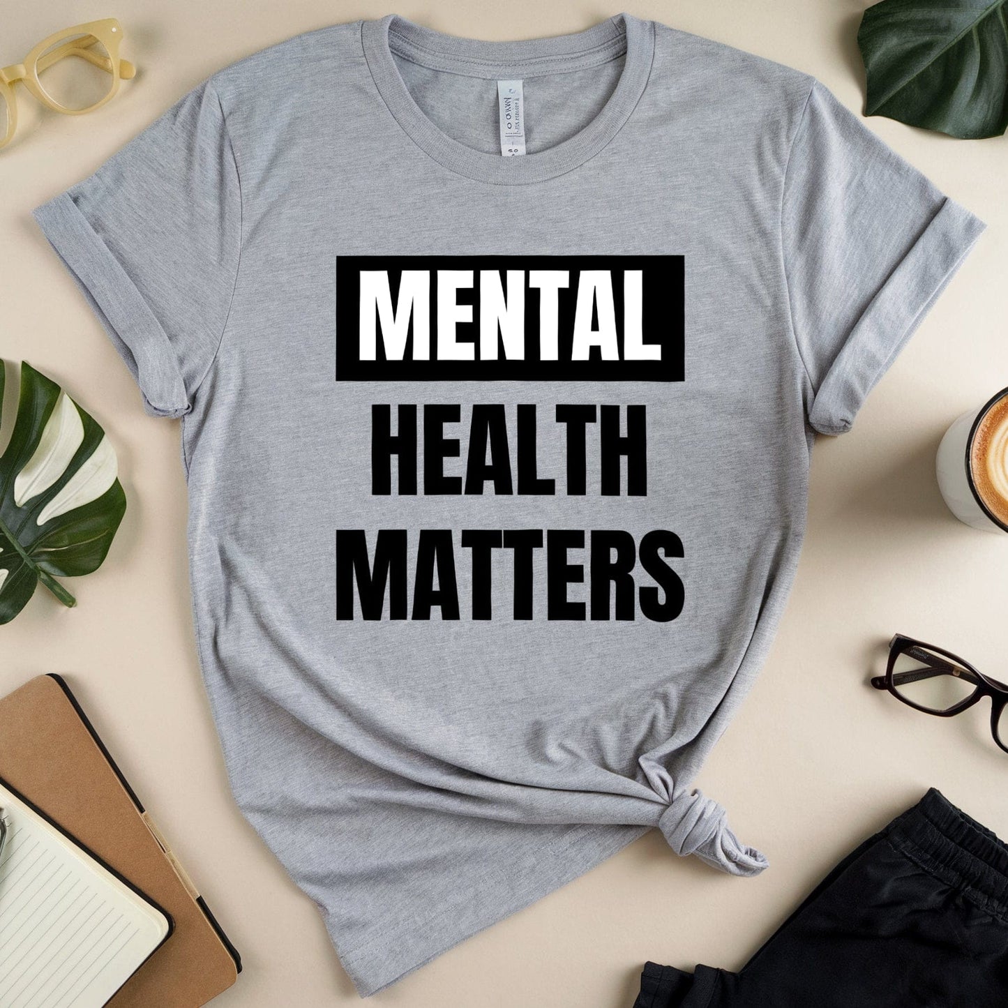Gray t-shirt with 'Mental Health Matters' text on a table with accessories