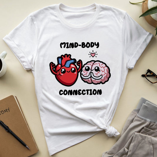 White t-shirt with a heart and brain graphic and text on a light surface with a notebook, coffee, and glasses.