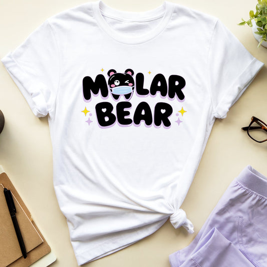 A white graphic t-shirt with a 'Molar Bear' cartoon bear design, styled in a flat-lay arrangement with lavender shorts, glasses, a notebook, a coffee cup, and a small potted plant on a light beige background.