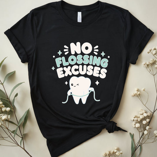 A black short-sleeve graphic T-shirt laid flat on a light beige background with dried flowers around it. The shirt has a front graphic that reads “NO FLOSSING EXCUSES” in white and mint green lettering, with a cartoon tooth holding a flossing cord and small sparkles.