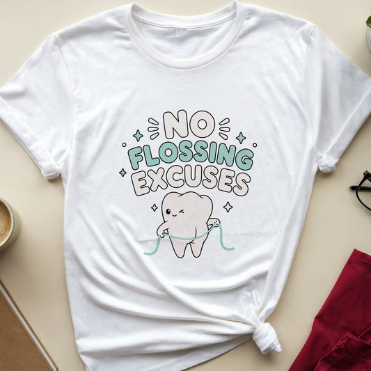 A white graphic t-shirt with a cartoon tooth and the text 'NO FLOSSING EXCUSES' is styled in a flat lay on a beige background, surrounded by a coffee cup, notebook, glasses, and folded red pants.