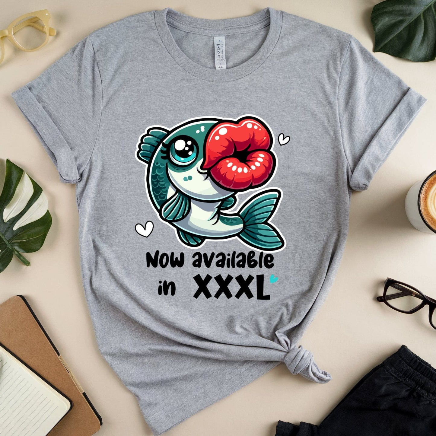 Gray t-shirt with a fish graphic and text on a beige surface with accessories.