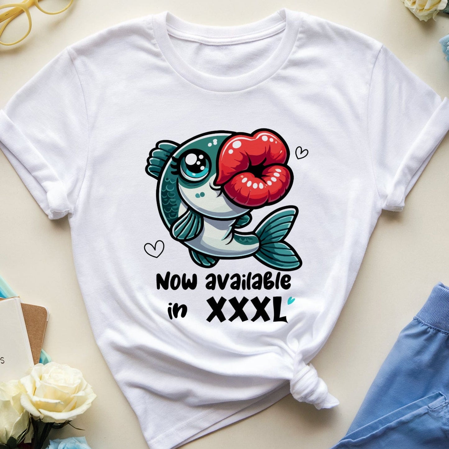 White t-shirt with a fish graphic and text on a light surface with flowers and a notebook.