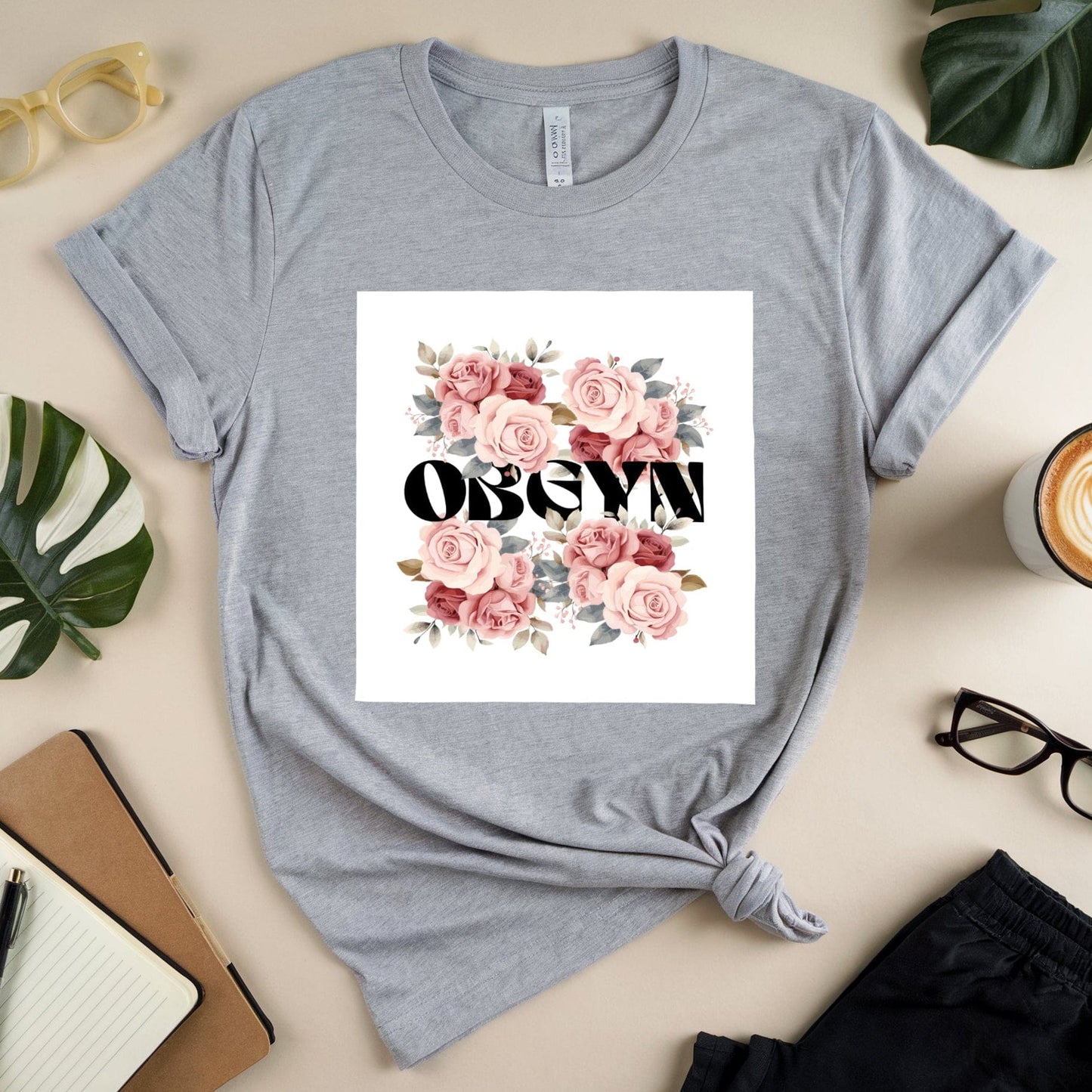Gray t-shirt with floral design and text on a beige surface with accessories.