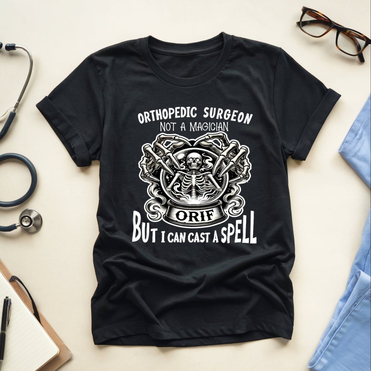 Black t-shirt with orthopedic surgeon graphic and text on a light surface with medical items.