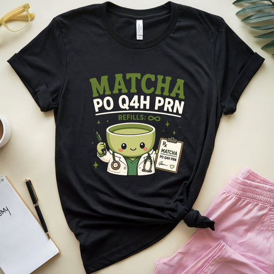 A black graphic t-shirt laid flat on a light beige surface, styled with a coffee cup, notebook, pen, yellow glasses, green leaves, and pink pants. The t-shirt features a cartoon matcha doctor and the text 'MATCHA PO Q4H PRN REFILLS: ©©'.