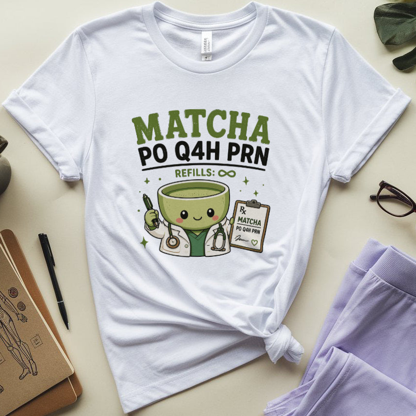 A white graphic t-shirt featuring a cute matcha bowl character and the text 'MATCHA PO Q4H PRN REFILLS: ∞' in green and black. The t-shirt is styled in a flat lay with lavender sweatpants, glasses, a notebook, a coffee mug, and a leaf on a light beige background.