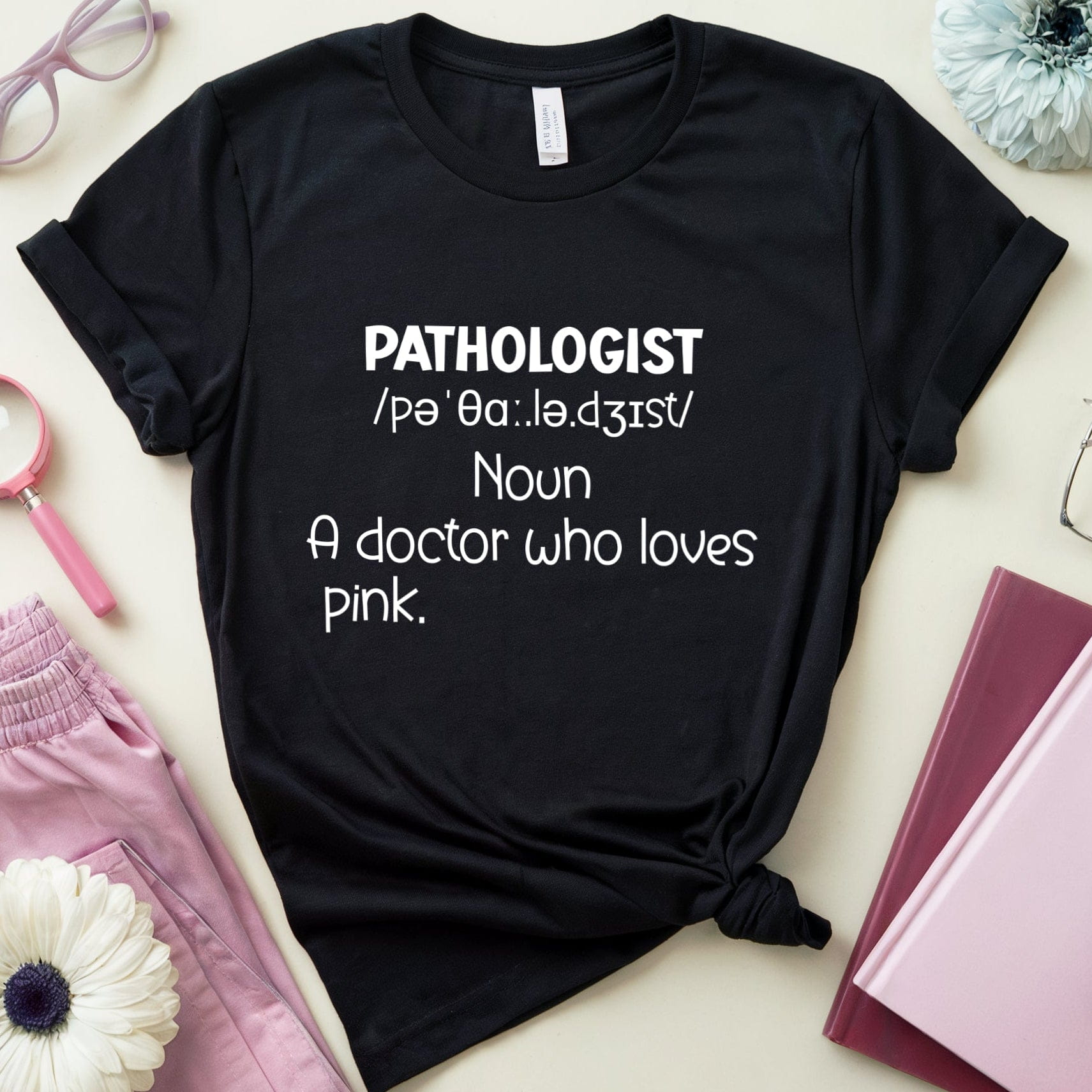 Black t-shirt with 'PATHOLOGIST' definition text on a light surface with accessories.