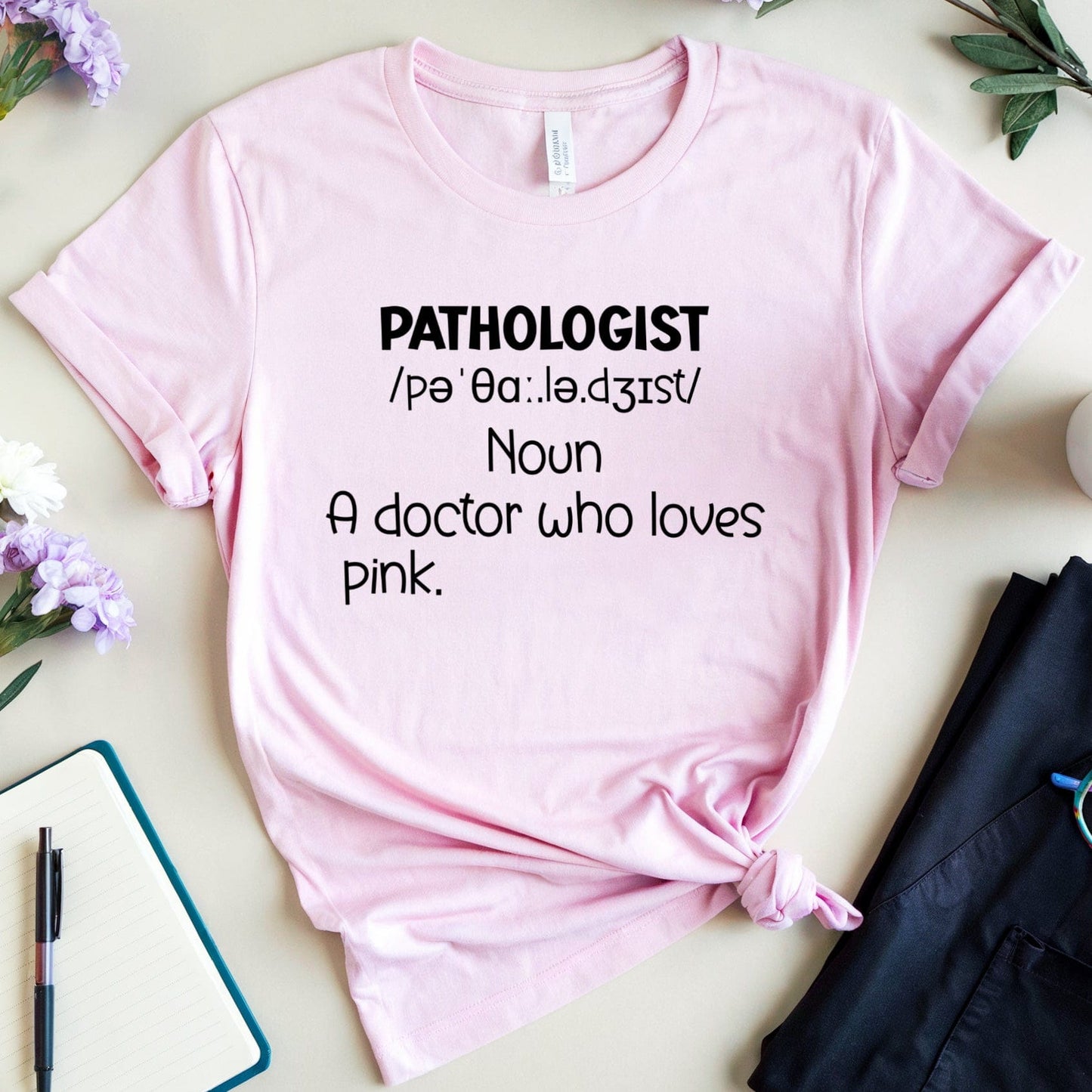 Pink t-shirt with text on a table with flowers and a coffee cup.