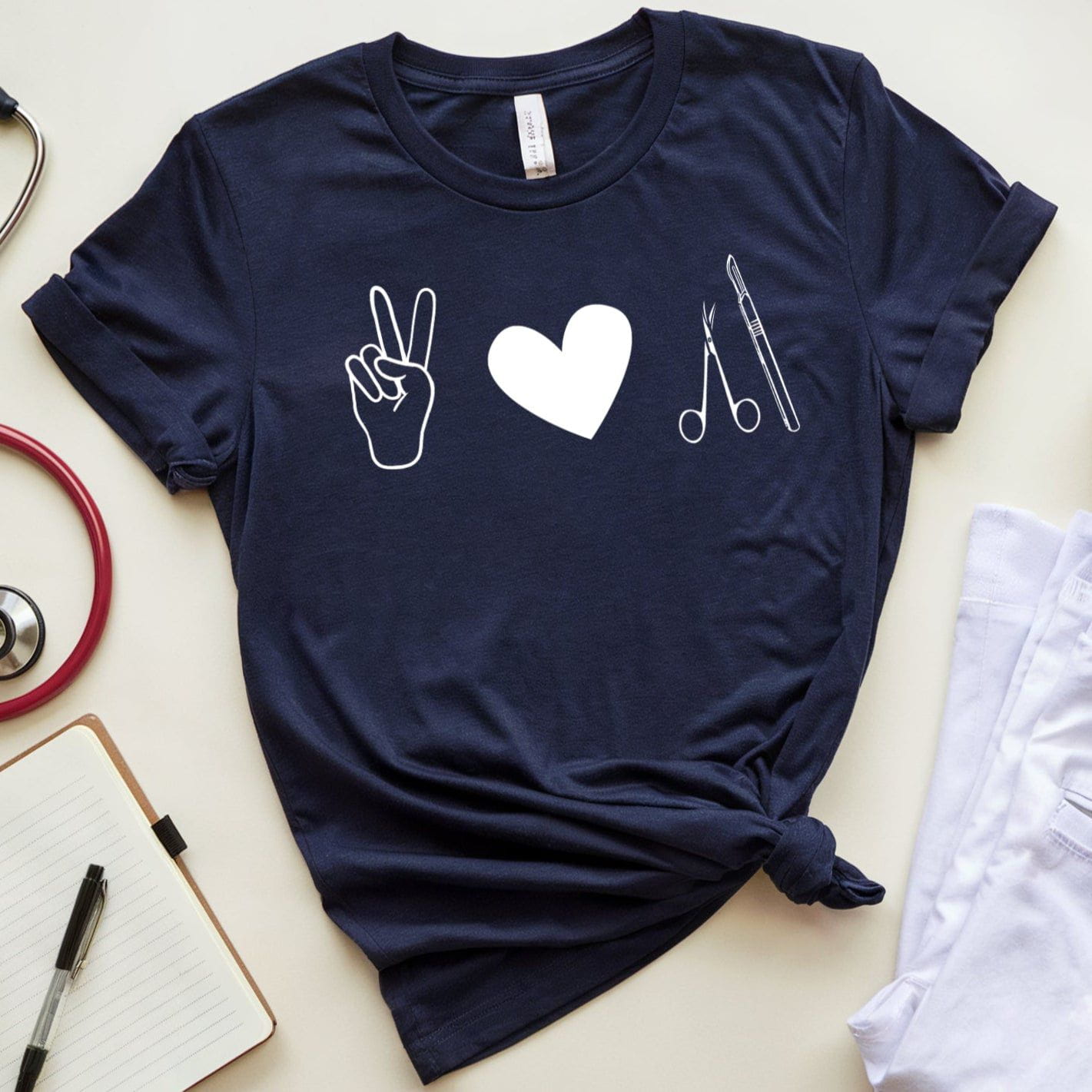 Navy blue t-shirt for surgeons with medical symbols on a light surface with stethoscope, coffee, and notebook.