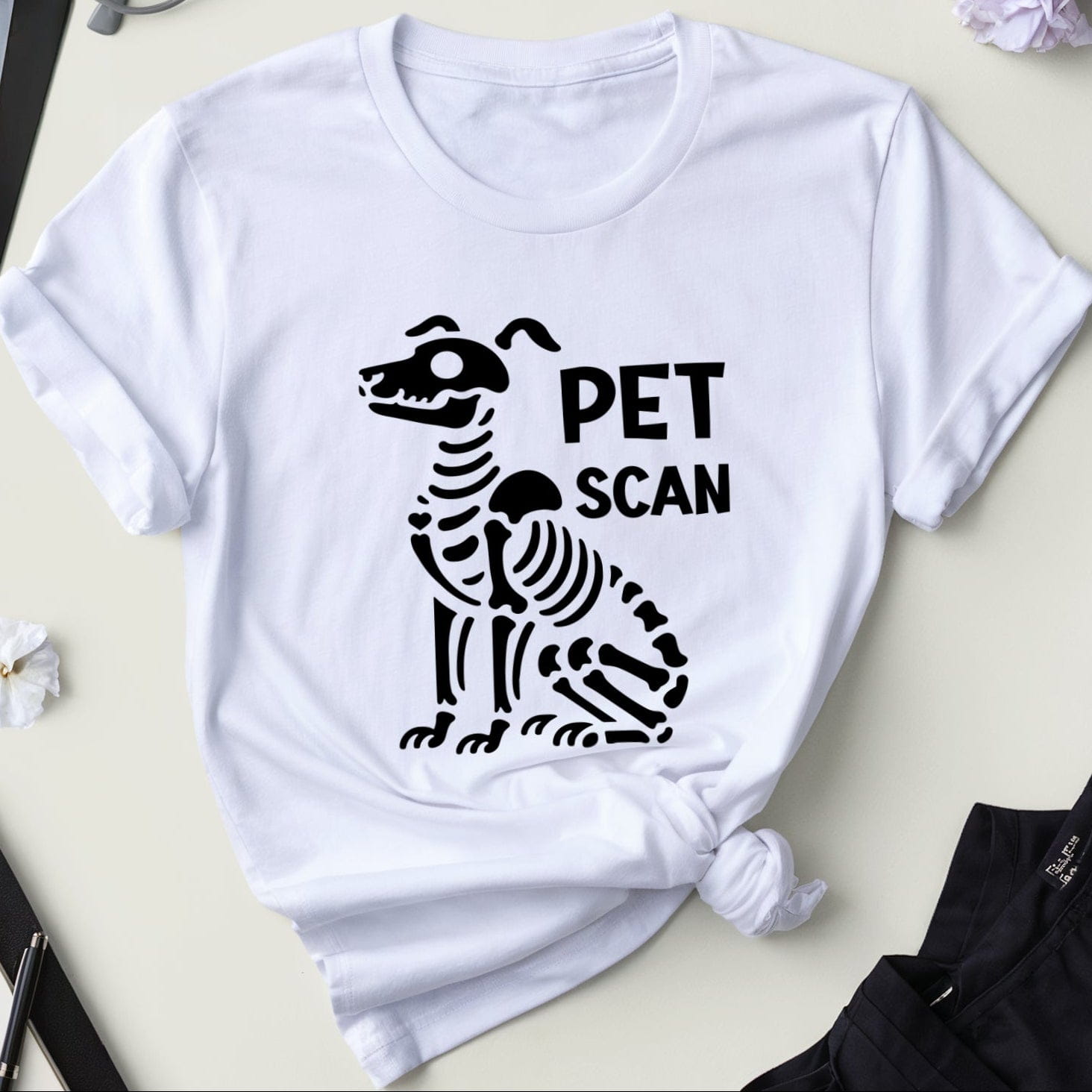 White t-shirt with black zebra skeleton design and 'PET SCAN' text on a light surface with medical-themed items.