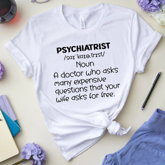 White t-shirt with 'PSYCHIATRIST' definition text on a light surface with accessories.