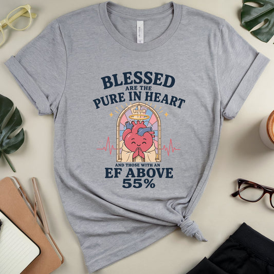 A heather gray graphic t-shirt with a heart-shaped illustration and the text 'Blessed are the Pure in Heart and those with an EF above 55%' displayed in a styled flat-lay with glasses, leaves, a notebook, and a coffee cup.