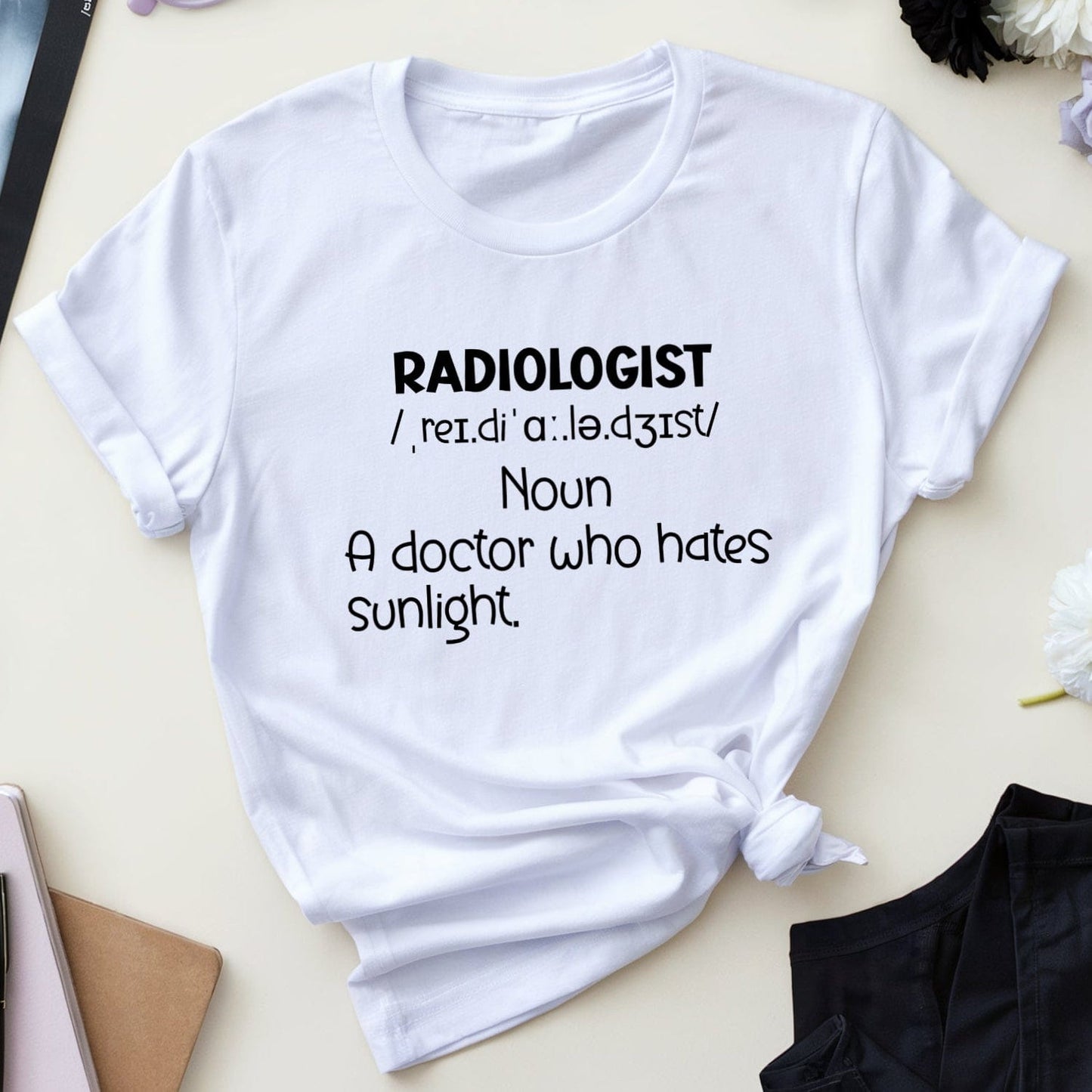 White t-shirt with 'Radiologist' definition text on a table with medical-themed items.