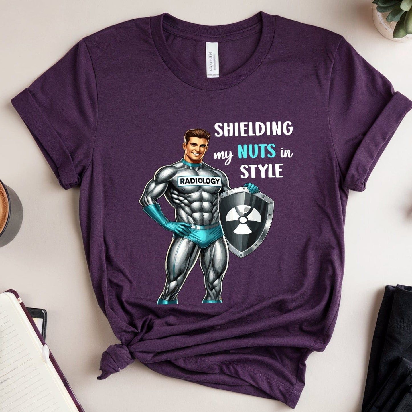 Purple t-shirt with superhero graphic and text on a table with a coffee cup and glasses.