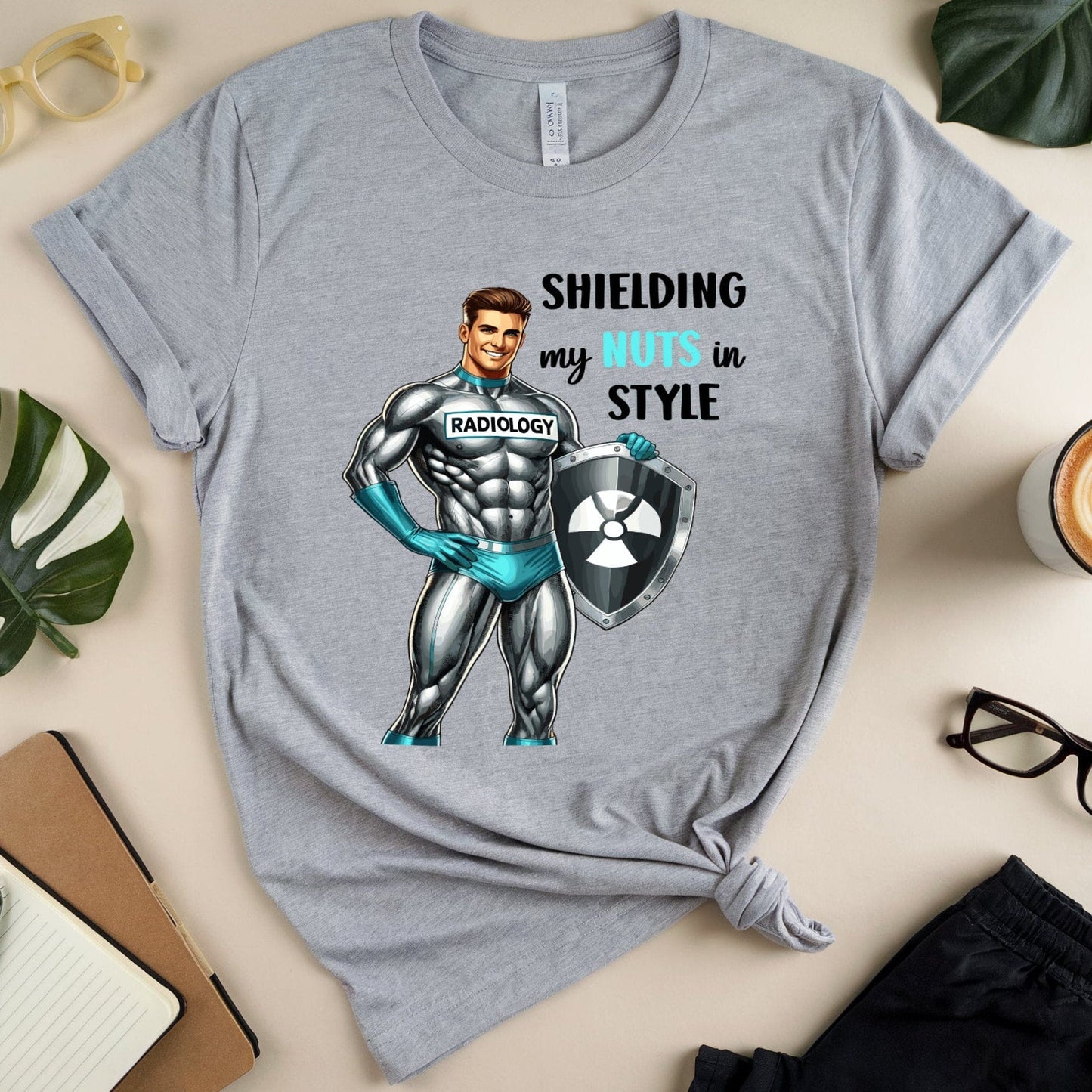Gray t-shirt with superhero graphic and text on a beige surface with accessories.