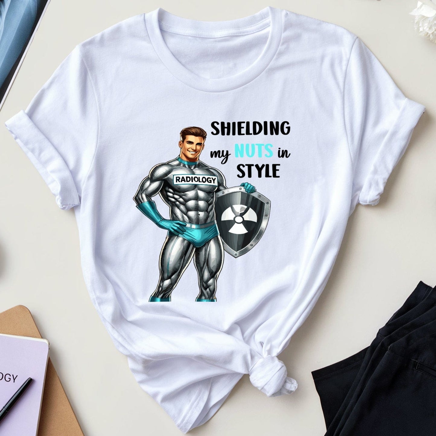 White t-shirt with superhero graphic and text on a table with medical books and flowers.