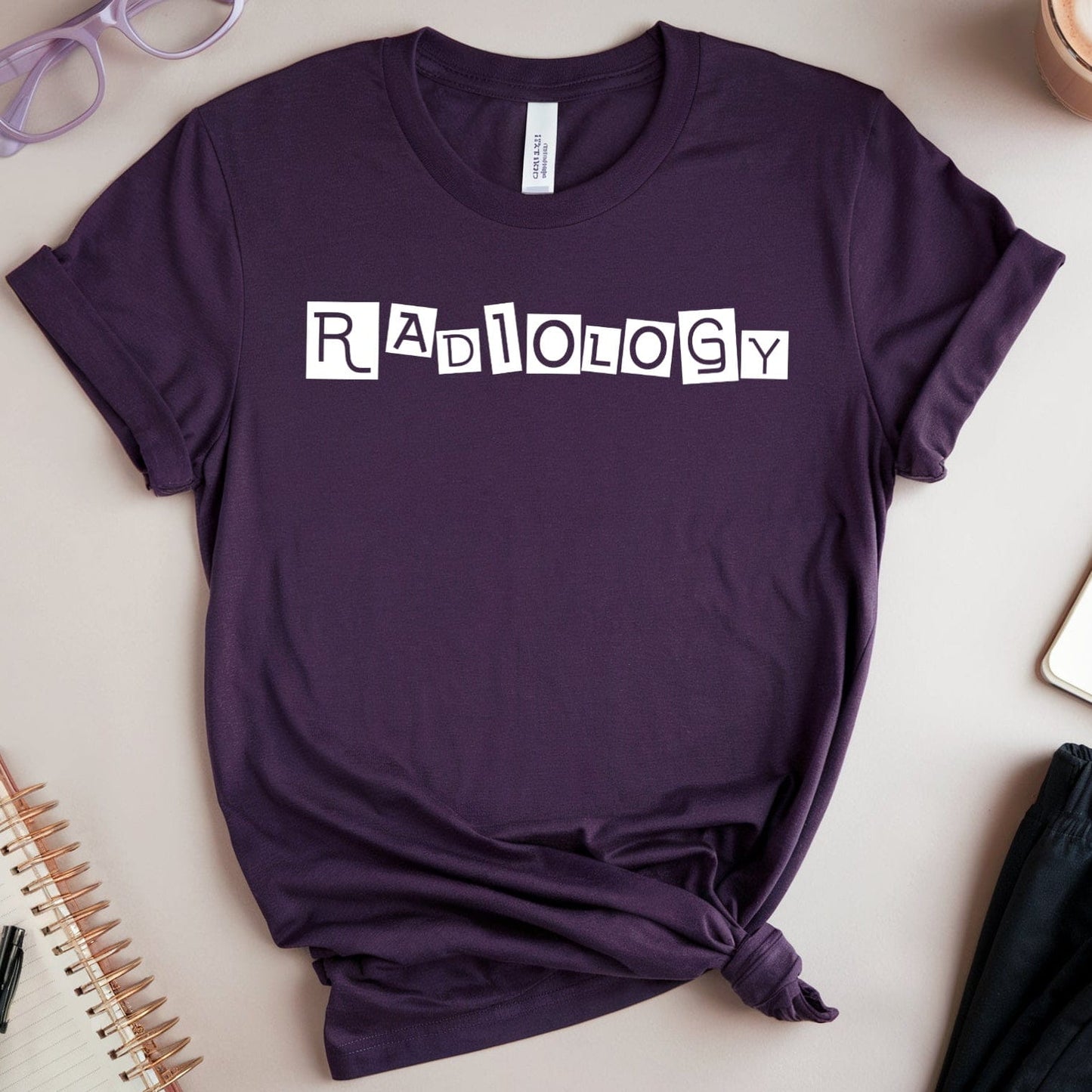 Purple t-shirt with 'Radiology' text on a light surface with accessories.