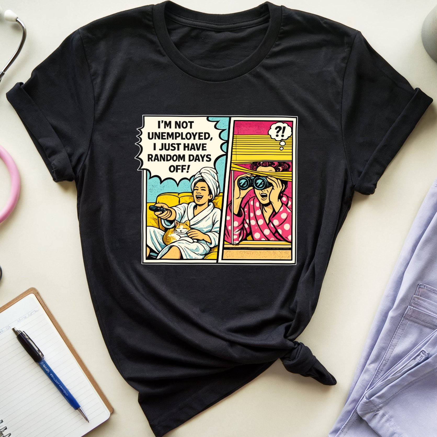Black t-shirt with a graphic design on a light surface with a stethoscope, notebook, and coffee mug.