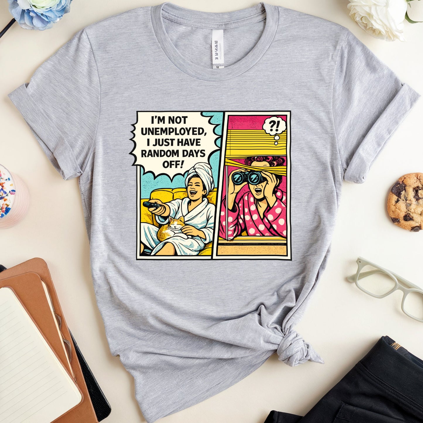 Gray t-shirt with comic-style graphic and text on a desk with office supplies.