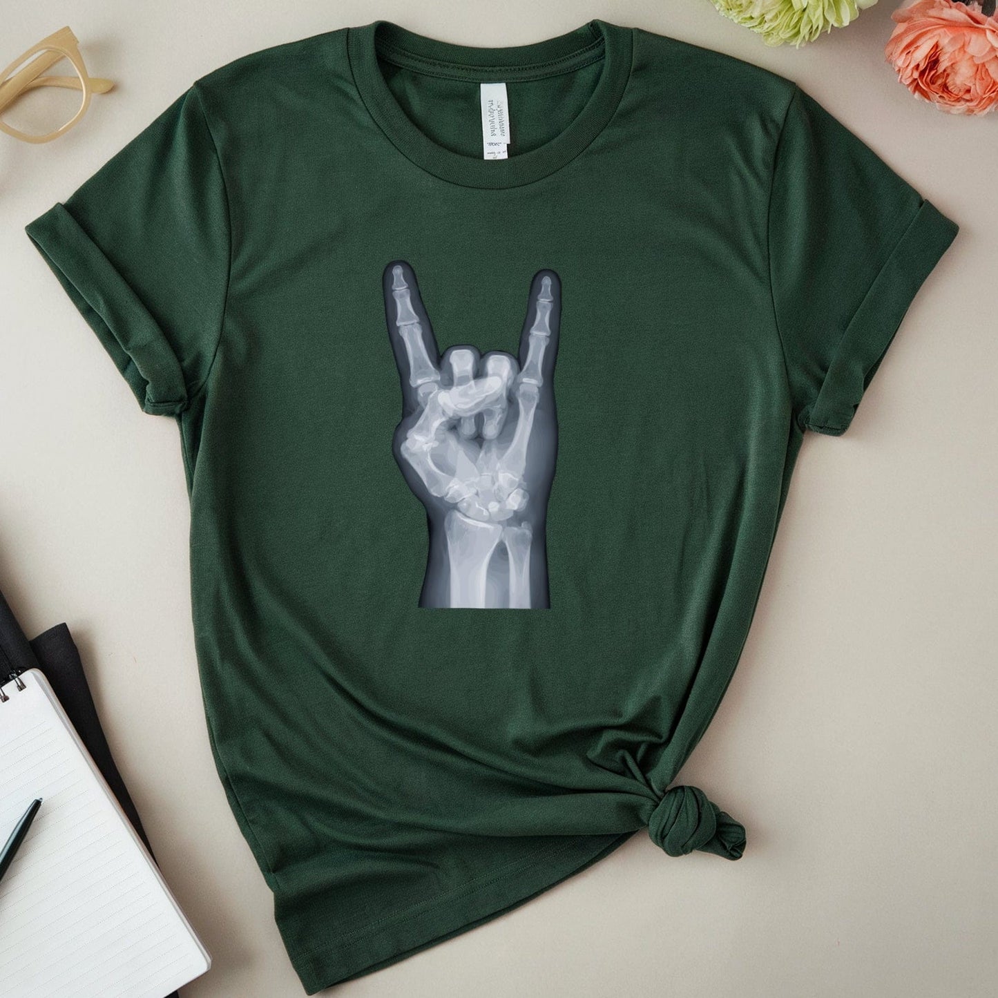 Green t-shirt with a hand graphic on a light surface with flowers and glasses.
