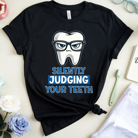 Black t-shirt with a tooth graphic and text on a light surface with flowers and dental-themed items.