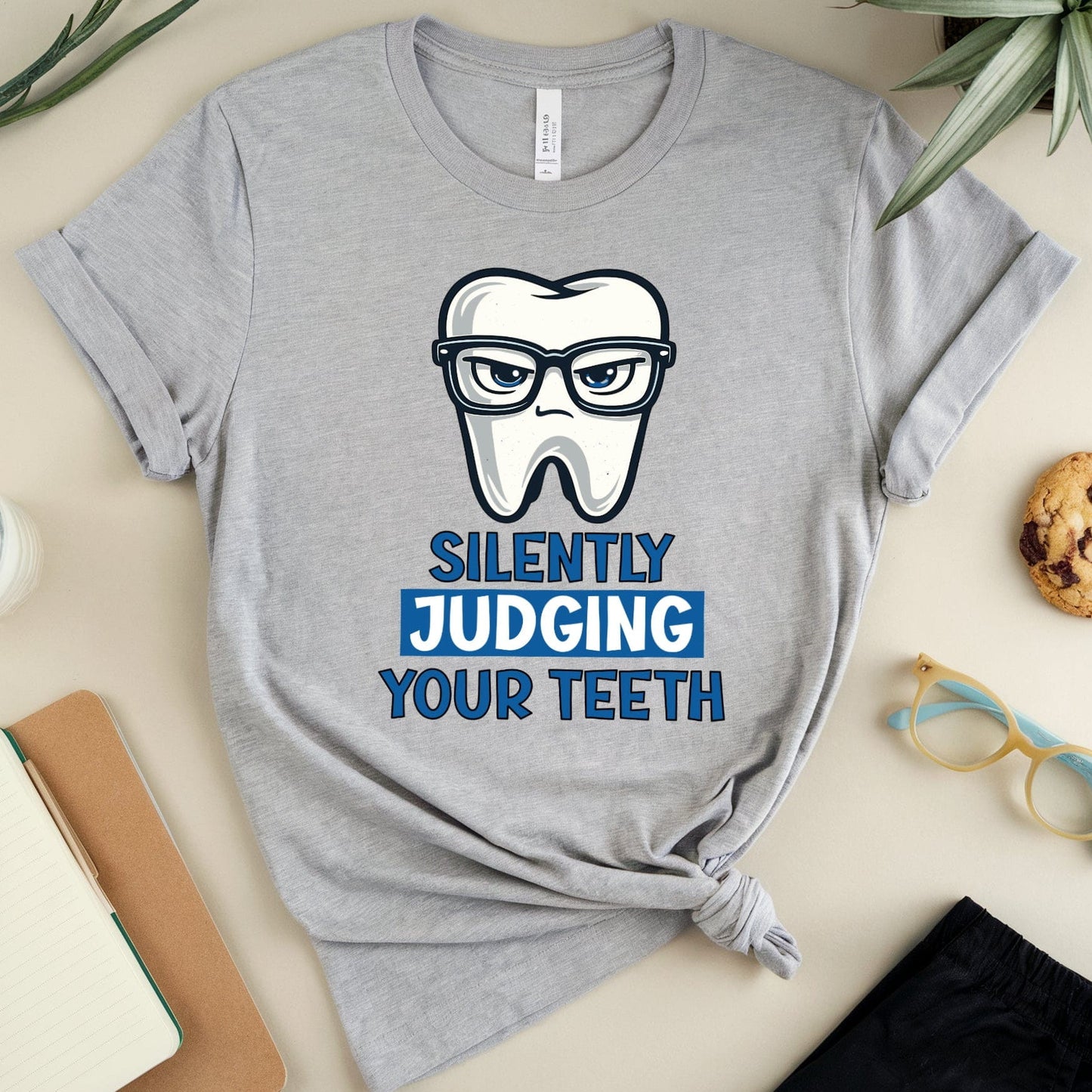 Gray t-shirt with a tooth graphic and text on a table with stationery items