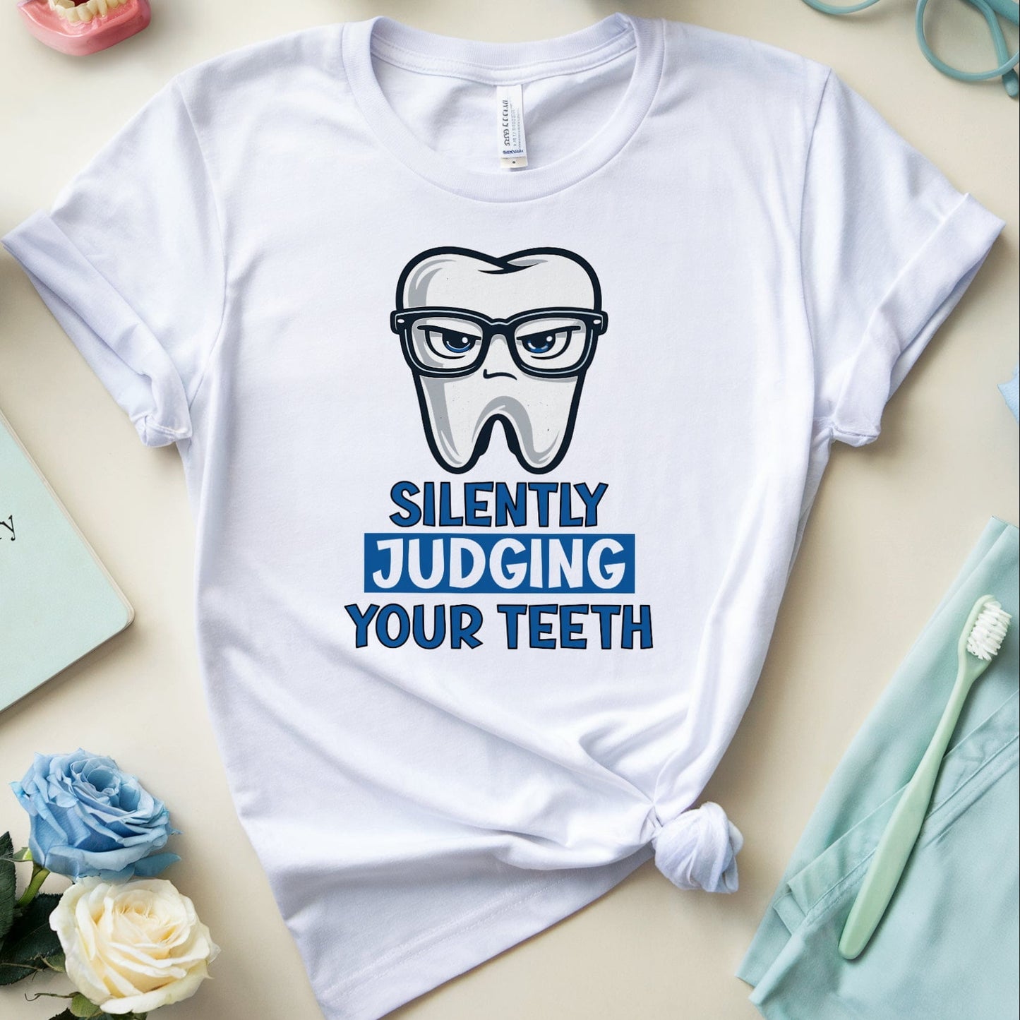 White t-shirt with a graphic design and text, surrounded by dental-themed items on a light surface.