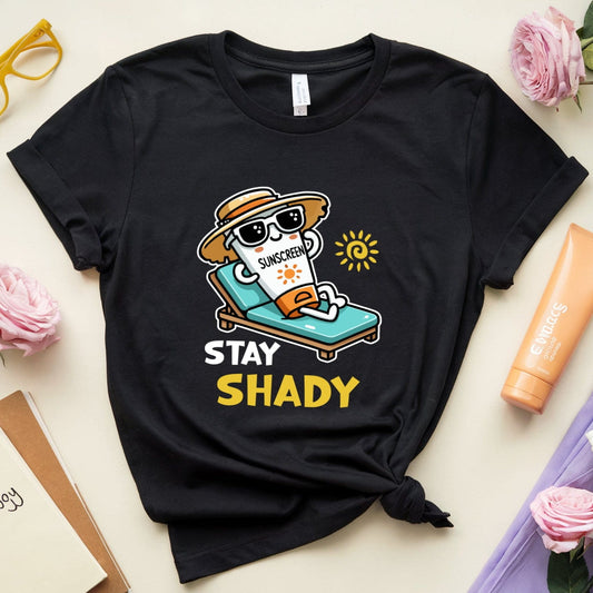 Black t-shirt with 'Stay Shady' graphic design on a light surface with flowers and sunglasses.