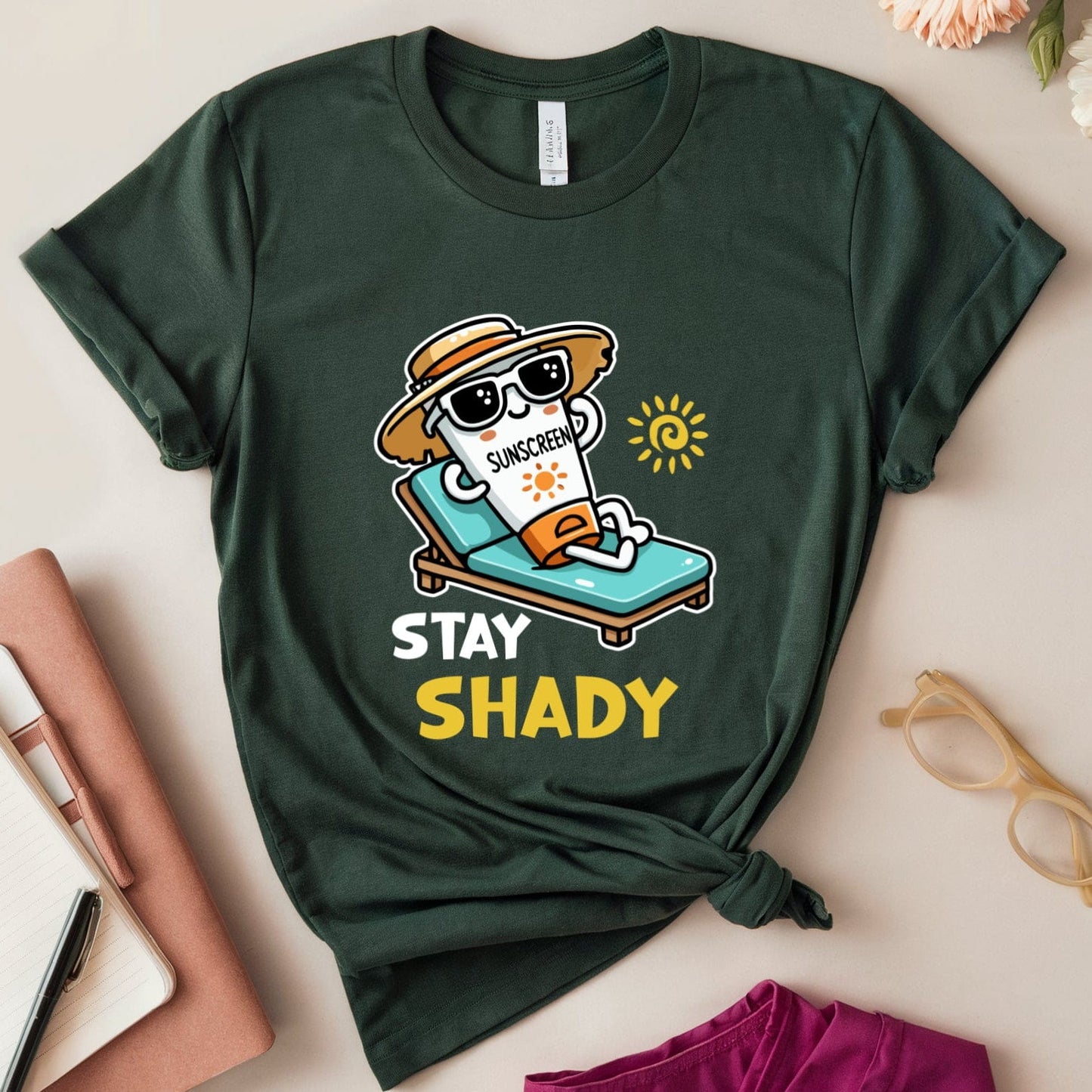 Green t-shirt with 'Stay Shady' graphic on a light surface with accessories.