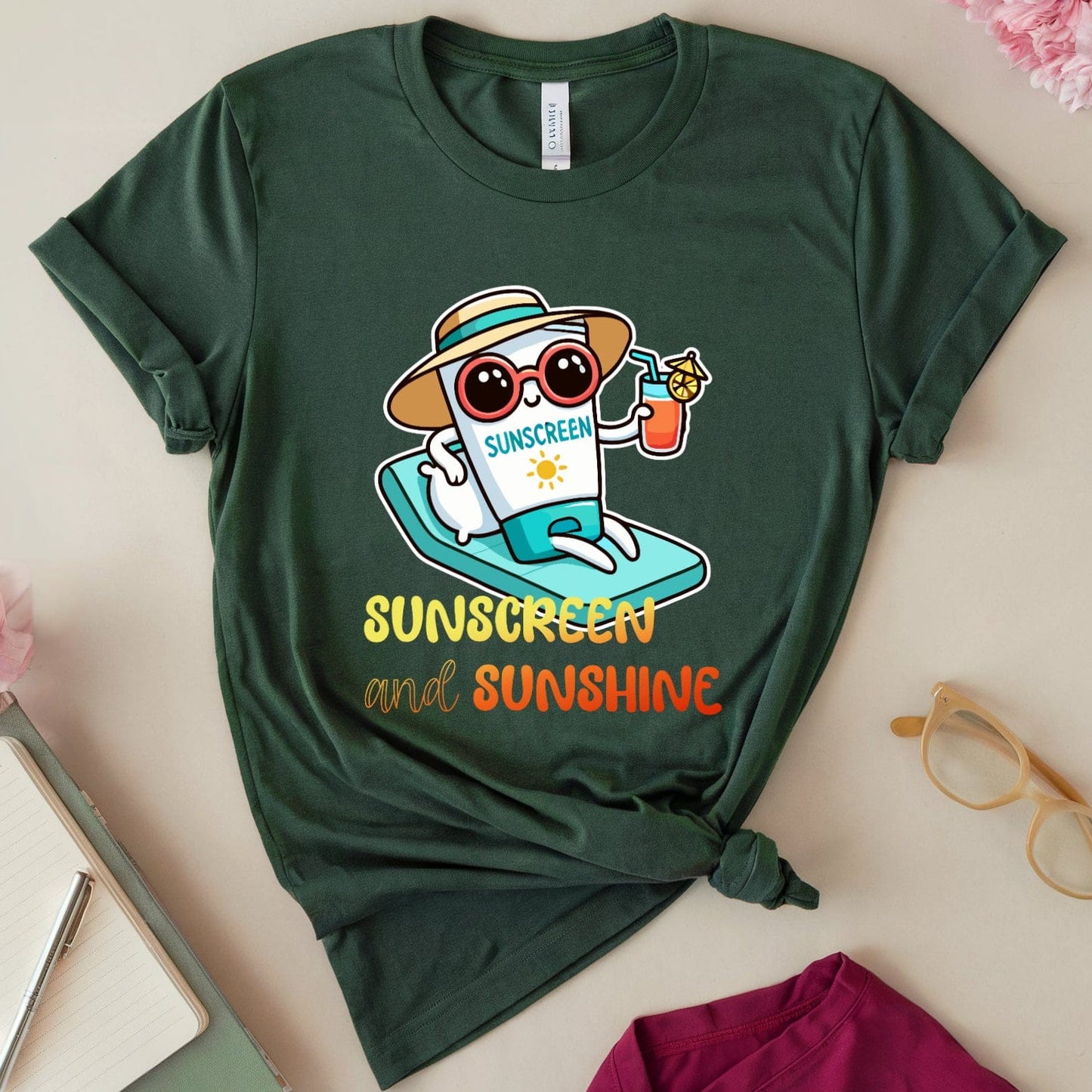 Green t-shirt with a cartoon character and 'Sunscreen and Sunshine' text on a light surface with flowers and glasses.