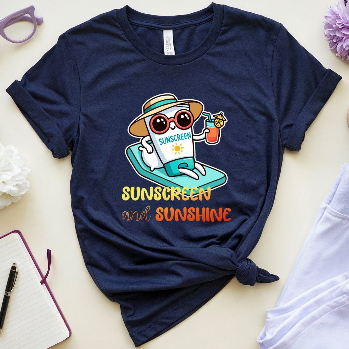 Navy blue t-shirt with a cartoon design and text 'Sunscreen and Sunshine' on a light surface with accessories.