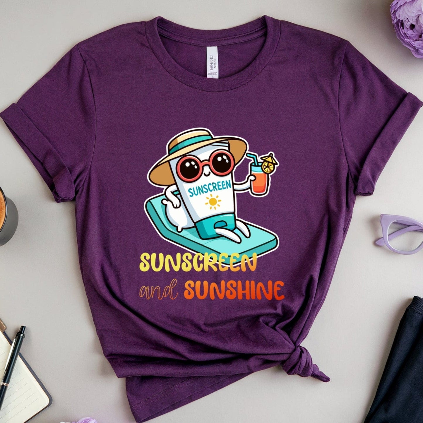 Purple t-shirt with a sun-themed design on a light surface with accessories.
