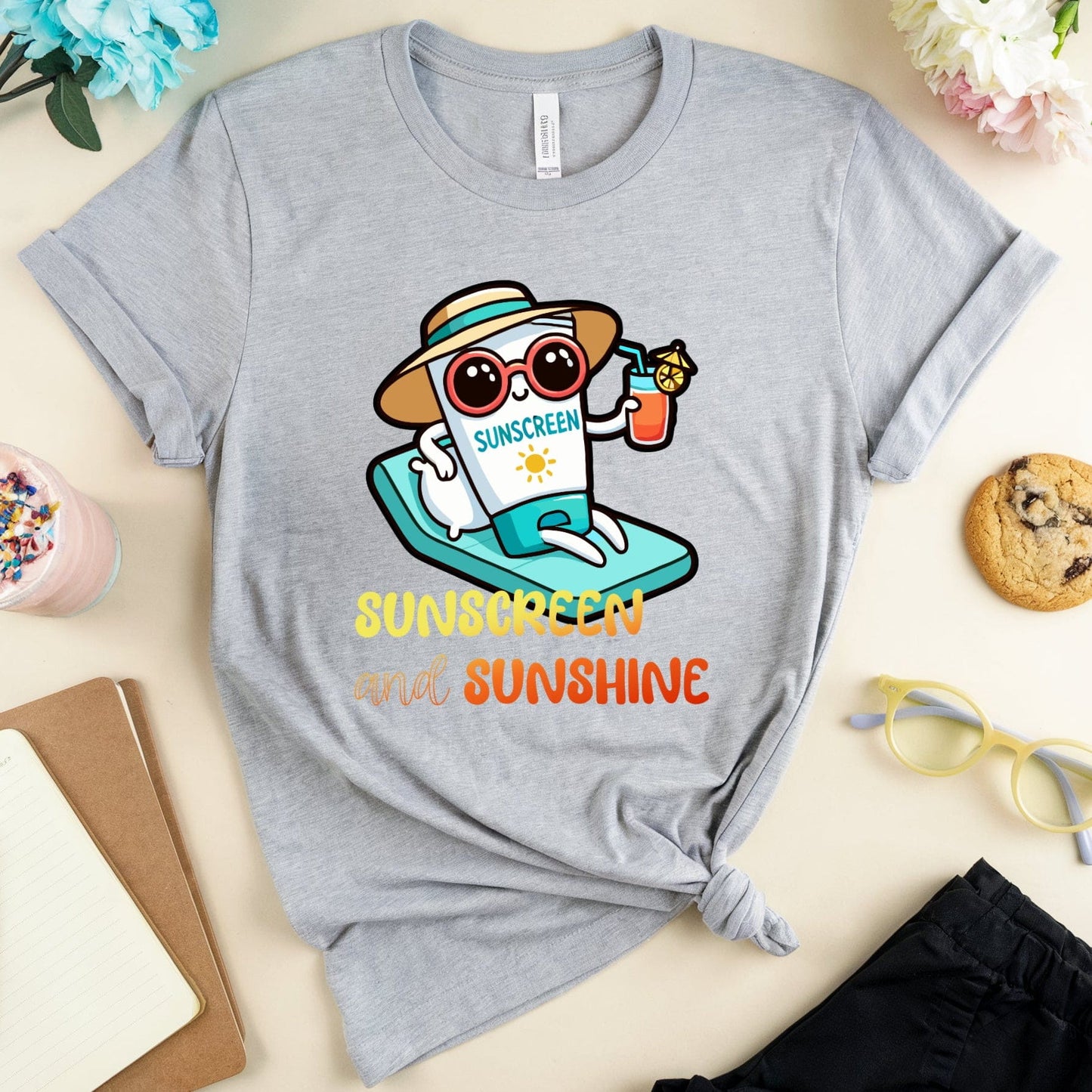 Gray t-shirt with a cartoon character and 'Sunscreen and Sunshine' text on a table with accessories.