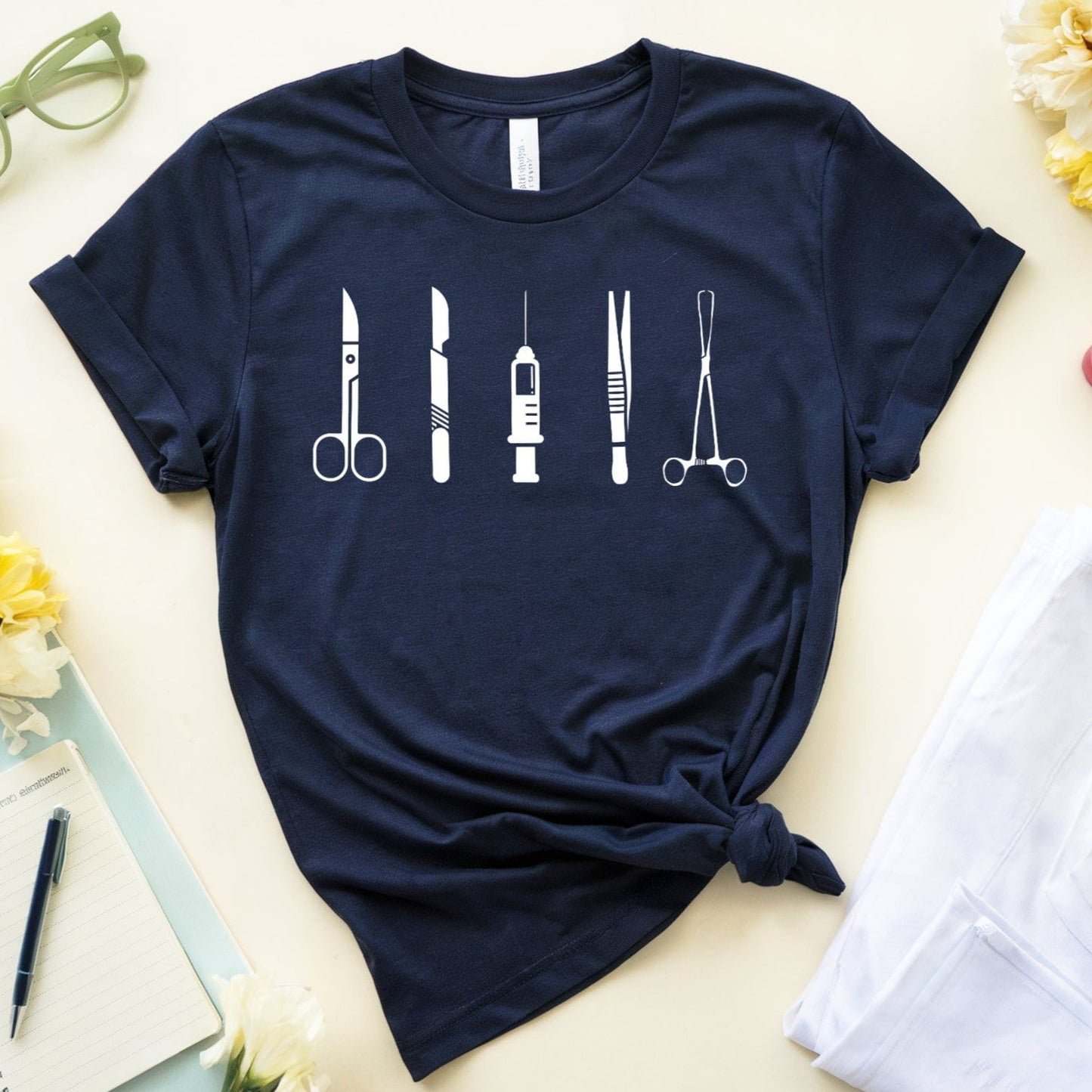 Navy blue t-shirt with medical tool designs on a light surface with flowers and stationery.