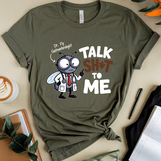 An olive green graphic t-shirt featuring a cartoon fly dressed as a doctor with the text 'TALK SH*T TO ME' and 'Dr. Fly Gastroenterologist'.