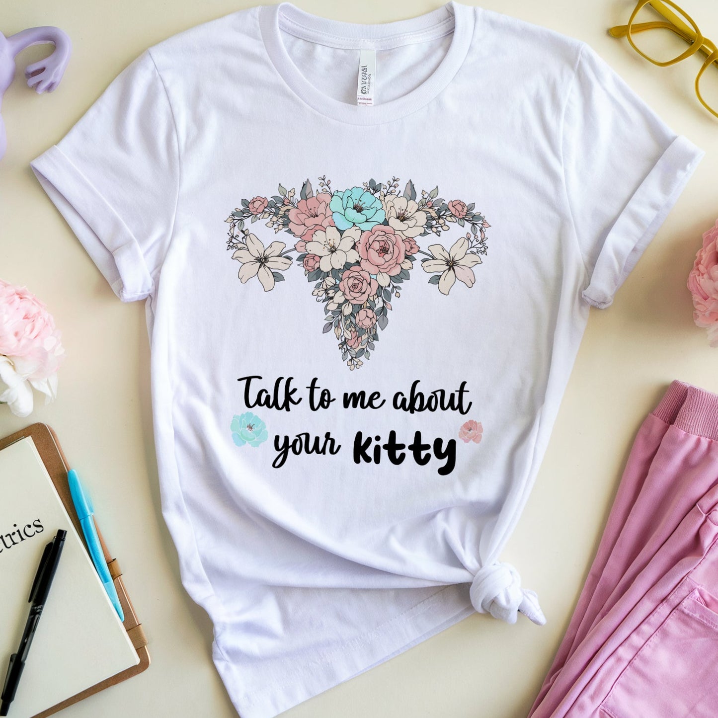 White t-shirt with floral heart design and text on a light surface with accessories.