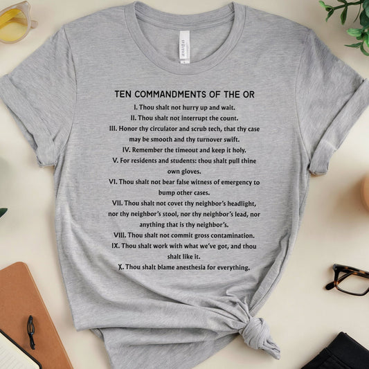 Gray t-shirt with 'Ten Commandments of the OR' text on a desk with office supplies.