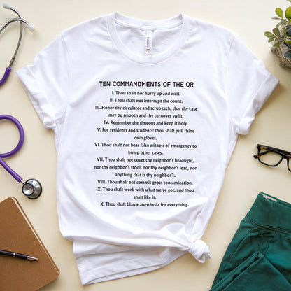White t-shirt with 'Ten Commandments of the OR' text on a light surface with medical supplies.