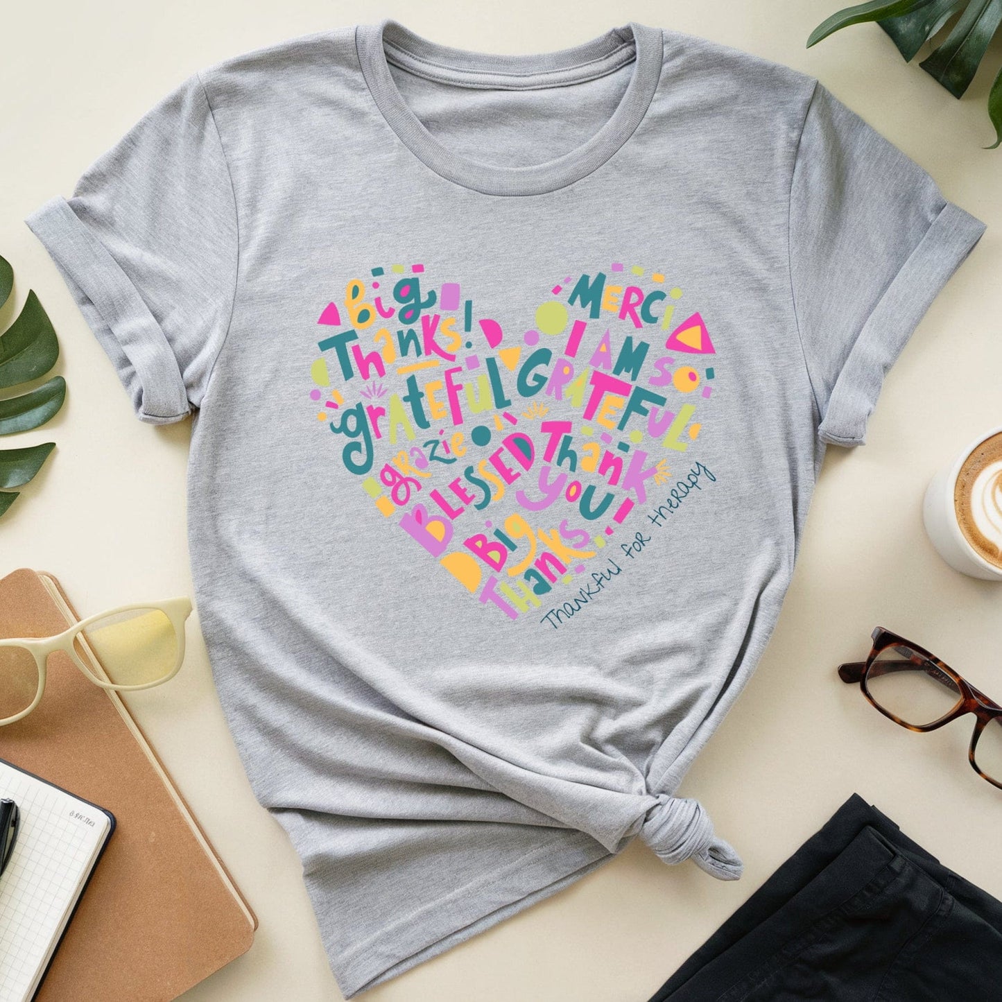 Gray t-shirt with colorful heart-shaped text design on a light surface with accessories.