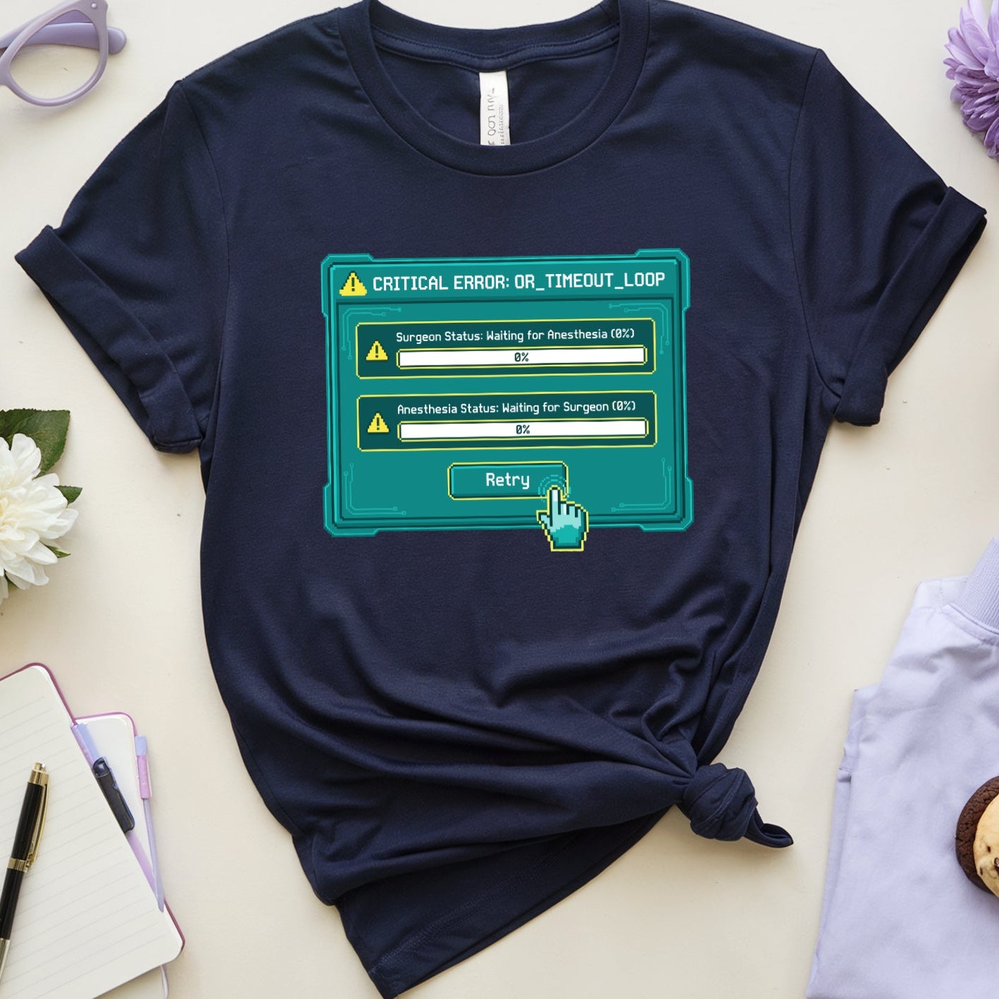 Navy blue t-shirt with a graphic design on a light surface with flowers and accessories.